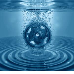 Esta imagen muestra un engranaje metálico sumergido en agua azul con burbujas visibles